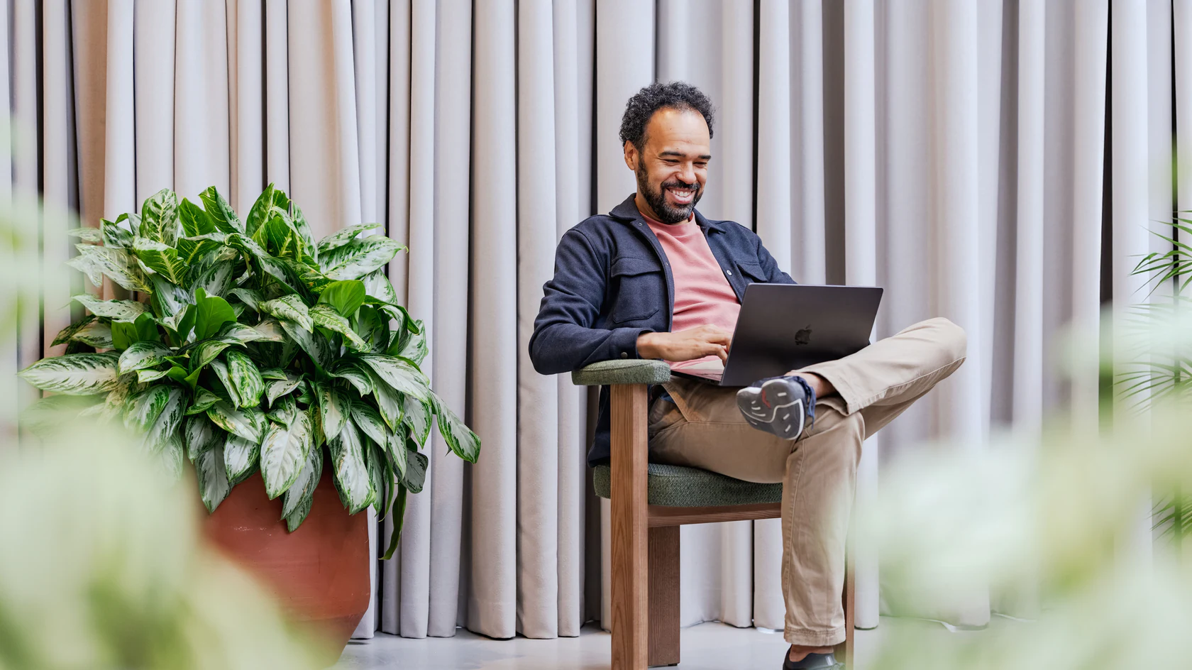 Kyle Welsworth in an armchair with a laptop on his knee beside a large plant